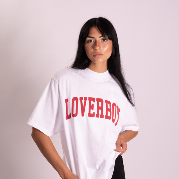 A woman modeling an oversized mockneck white t-shirt with 'LOVERBOY' printed in red arched block letters across the chest, set against a solid background.
